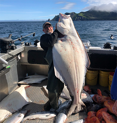 Captain Shane of Driftwood Charters in Homer, Alaska holds up a 180 pound Barndoor size halibut